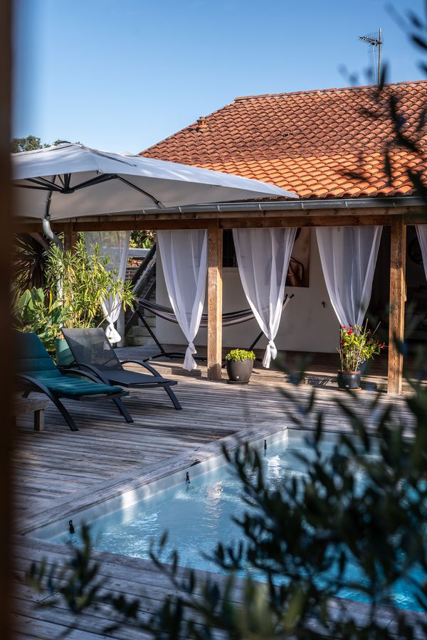 Beheizter Pool mit Sonnenliegen vor der Pergola mit weißen Vorhängen